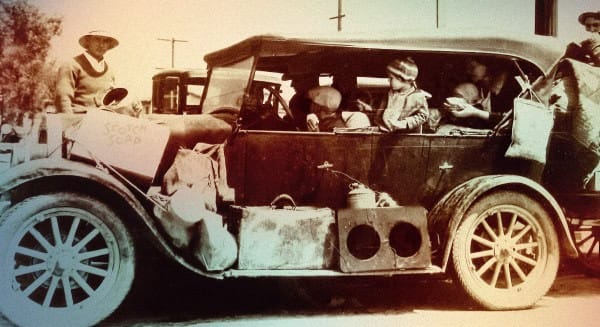 Old vintage car loaded with people, likely from the early 20th century, with a sign reading "Scrap" on the side, capturing historical transportation and social scenes.