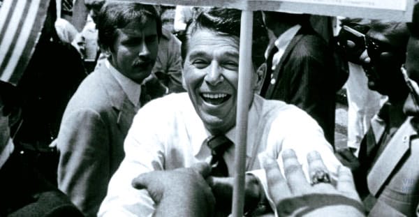 Photograph of John F. Kennedy smiling and engaging with supporters during a historical political rally.