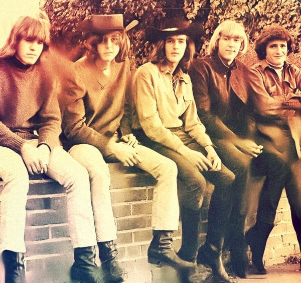 Vintage photo of iconic 1960s rock band wearing casual clothing, sitting outdoors against a brick wall, capturing the essence of music history and legendary sound archive.