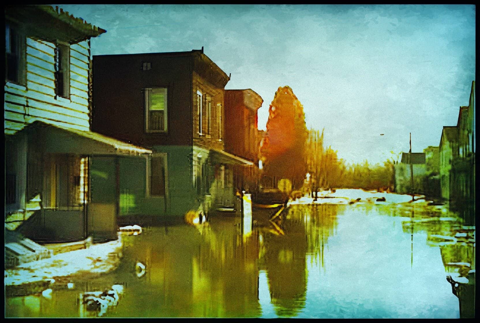 Flooded street with residential houses reflected in water, vibrant autumn colors, peaceful neighborhood, scenic landscape, urban flood aftermath, calm water surface with floating debris, community resilience.