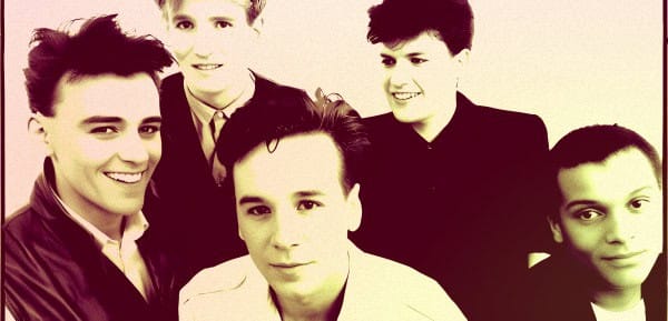 A black and white photo of a band with five members, showcasing classic 1980s hairstyle and fashion, representing music history and cultural nostalgia.