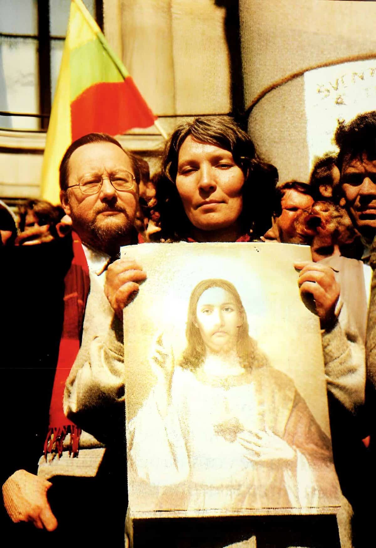 Protesters holding an image of the Virgin Mary during a demonstration, reflecting historical and religious news coverage, with a yellow and red flag in the background, capturing a moment of social and cultural relevance.