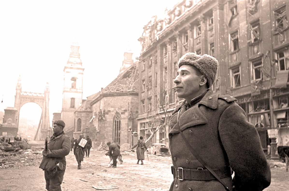Deserted war-torn city street during WWII with soldiers and damaged buildings, historical archive photo.