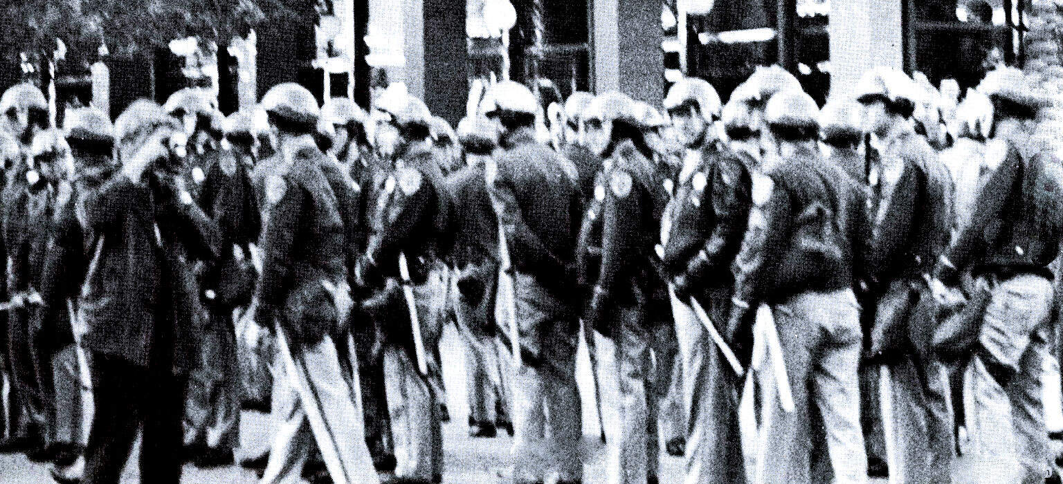 Police officers in riot gear standing in formation during protest or civil unrest, black and white historic photo, law enforcement and social history, newsroom, news archive, past daily archive.