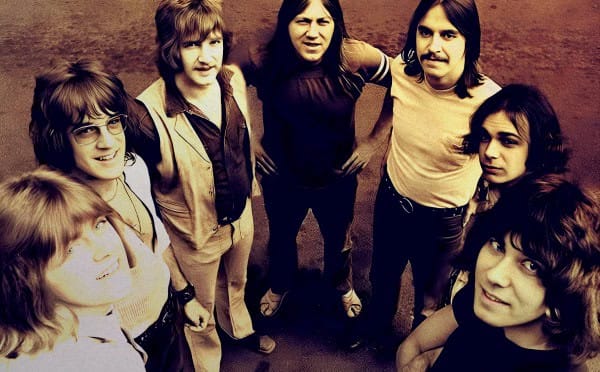 1970s rock band members standing outdoors, vintage style, promoting classic music and music history.