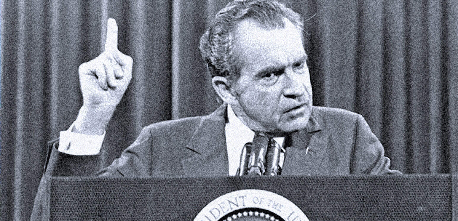 Detailed black and white photo of a man at a podium with the presidential seal, making a point with his raised finger during a speech or press conference.