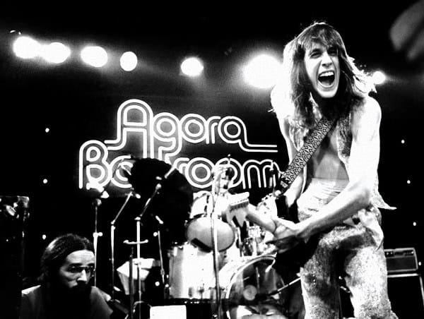 A woman passionately playing electric guitar on stage during a live concert at Agra Ballroom, with a vibrant atmosphere and dynamic performance captured in black and white.