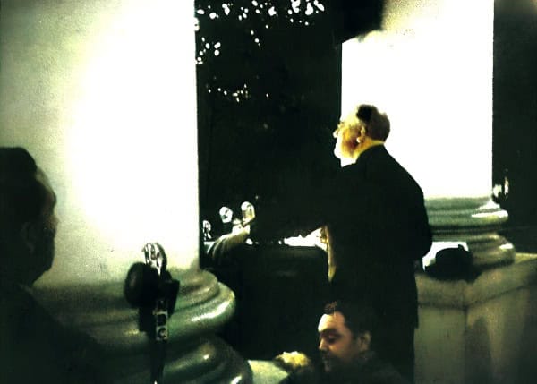 Old black and white photo of a man in a suit speaking inside a historic government building, with classical columns.
