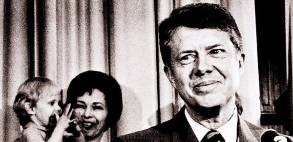 Vintage black and white photo of John F. Kennedy smiling, with Jacqueline Kennedy and a young child, capturing an iconic moment in American political history and presidential legacy.