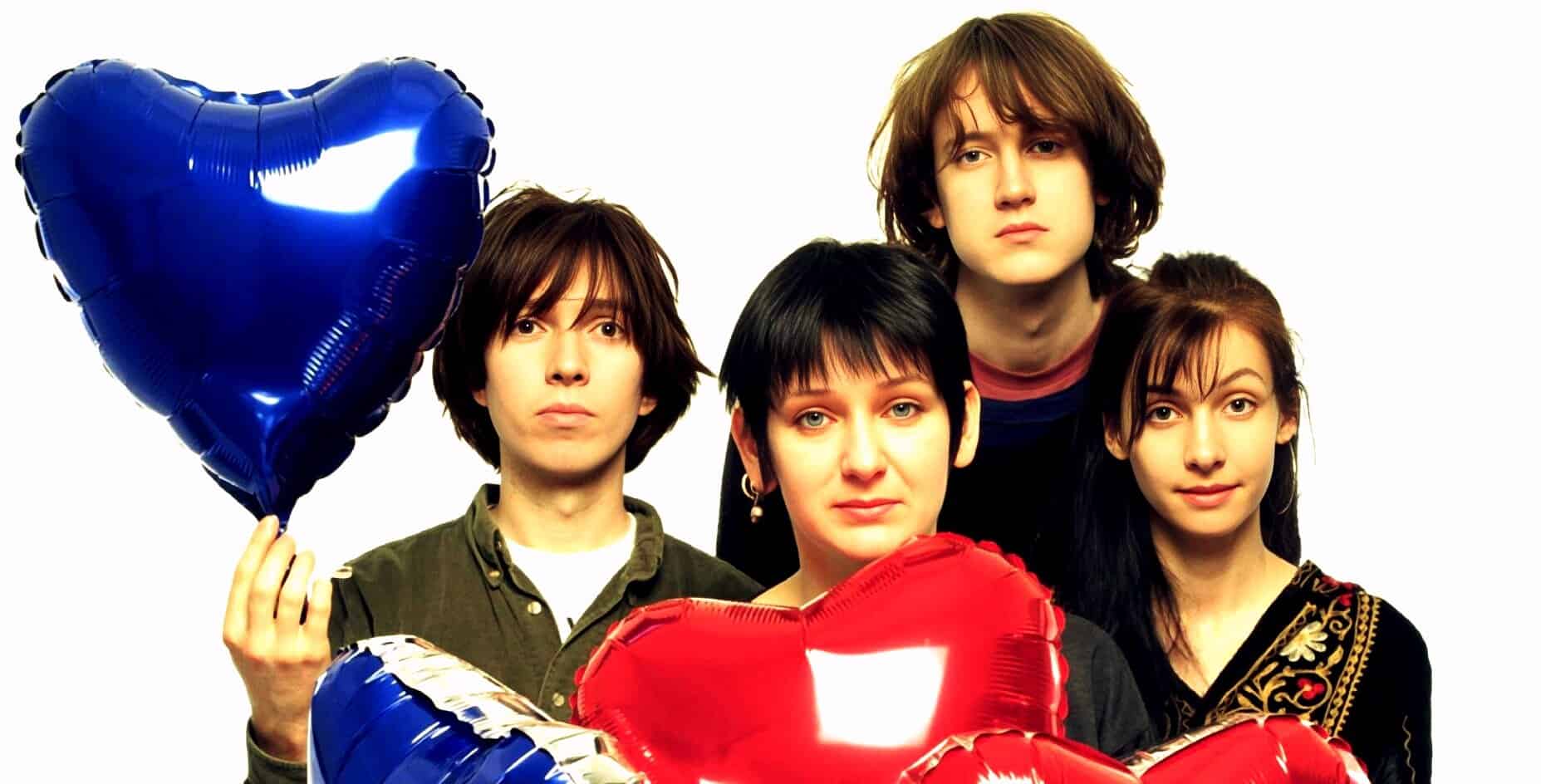 Young group of people holding red and blue heart-shaped balloons, symbolizing love or celebration, with a focus on unity and friendship, set against a white background for promotional or commemorative purposes.