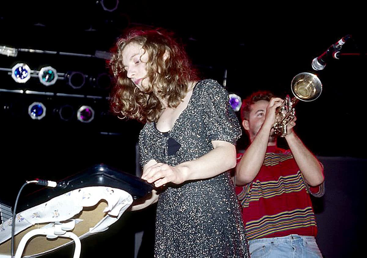 Electronic music performance with female DJ and trumpet player live on stage at a music event.