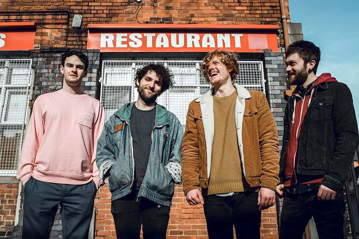 Nightlife, urban scene, young men, city street, casual fashion, four friends, brick building, outdoor gathering, city life, trendy attire, smiling, social event, youthful energy, street photography, friendship.