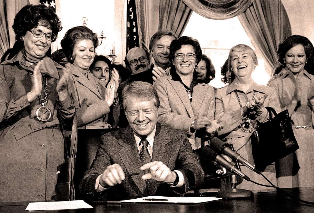 Historic political event photo with President John F. Kennedy signing legislation surrounded by women officials. Iconic moment captured in black and white emphasizing news, history, and political archives.
