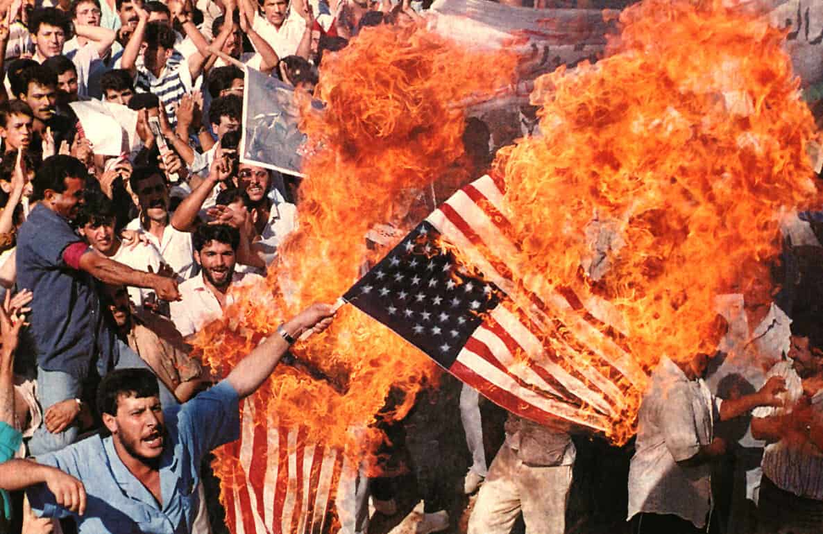 Burning American flag protest, political demonstration with fiery flag, anti-American protest image, historic news and music archive, impactful protest photo for news archives and history.