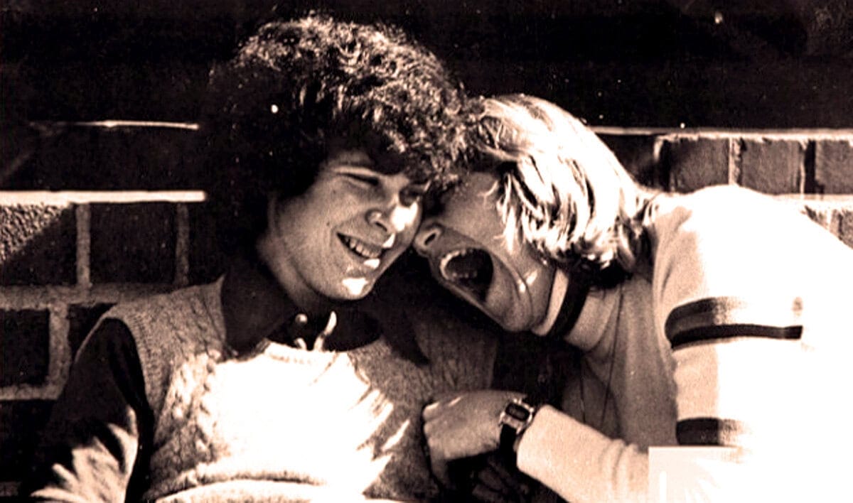 Young people laughing together, friendship, social interaction, happiness, carefree youth, casual clothing, outdoor brick wall background, black-and-white photo, candid moment, nostalgic vibe, community, bonds.