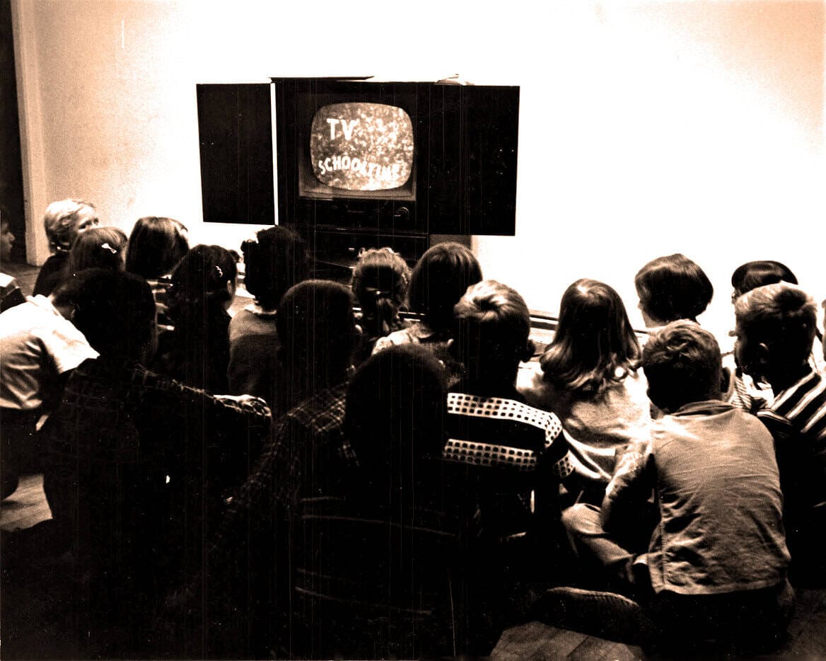 Kids watching television in a classroom or community center, vintage black and white photo, early TV broadcast, educational media, TV show for children, historical media archive, past daily sound archive.