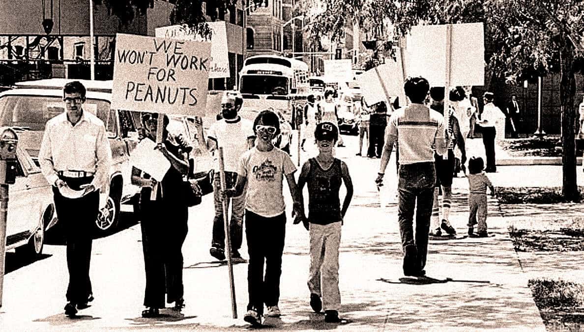 Protest march with diverse group holding signs for social justice, including "We Won't Work for Peanuts," demonstrating activism and community involvement.