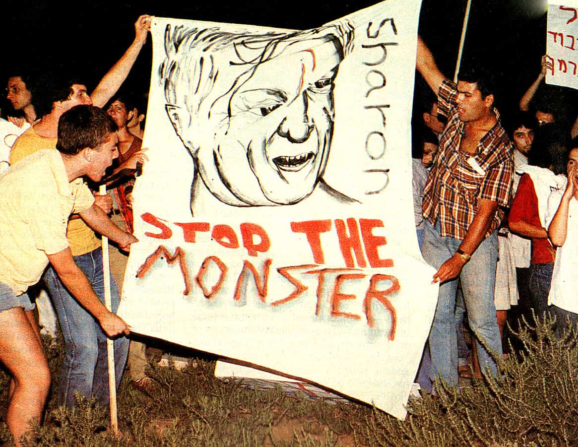 Young protesters holding a large handmade sign with a caricature and the message "Stop the Monster" during a demonstration against nuclear weapons or government policies.