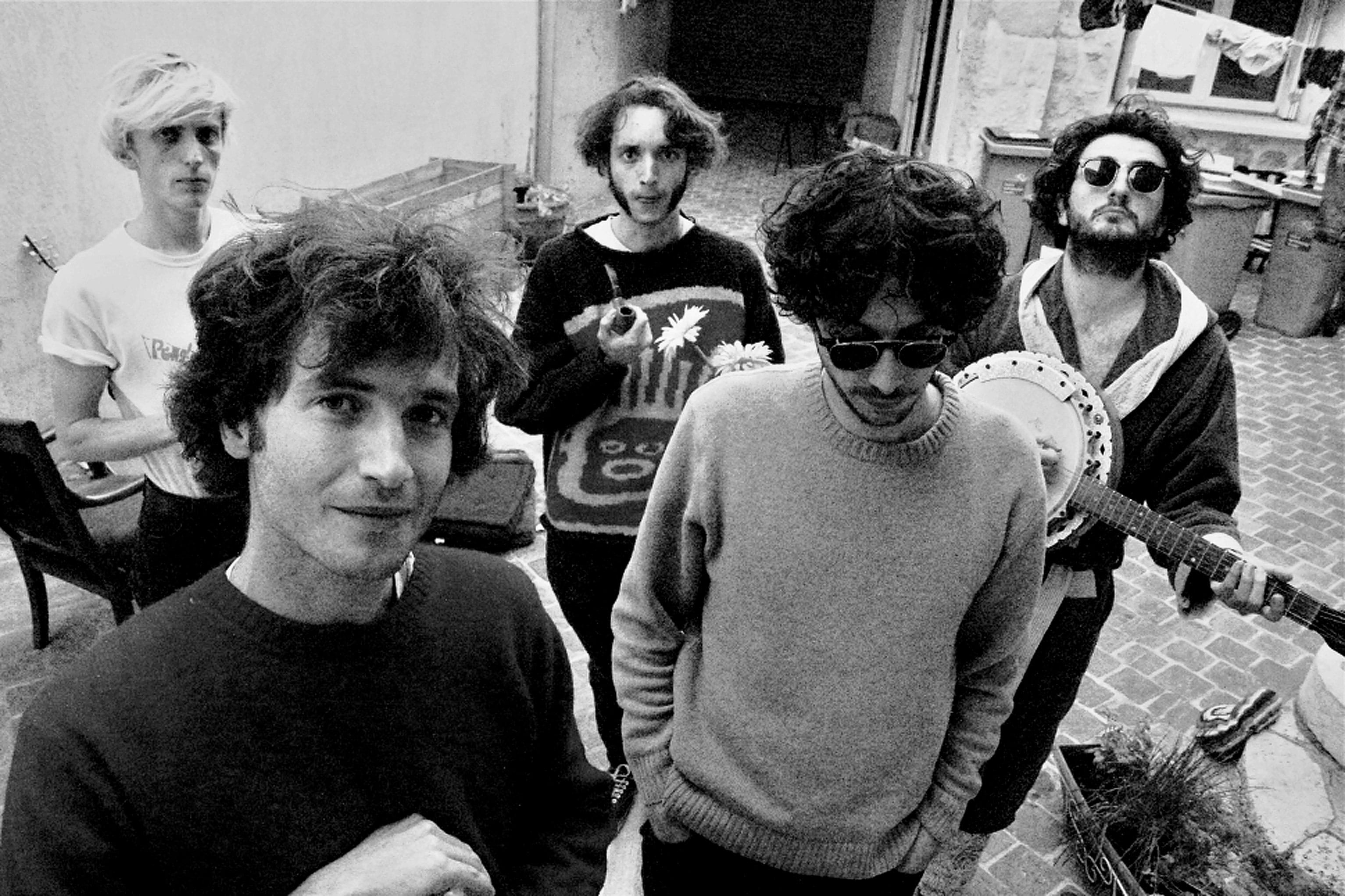 Vintage black and white photo of a band in a cozy studio, featuring musicians with guitars and microphones, capturing a historic moment of music and sound recording for an audio archive.