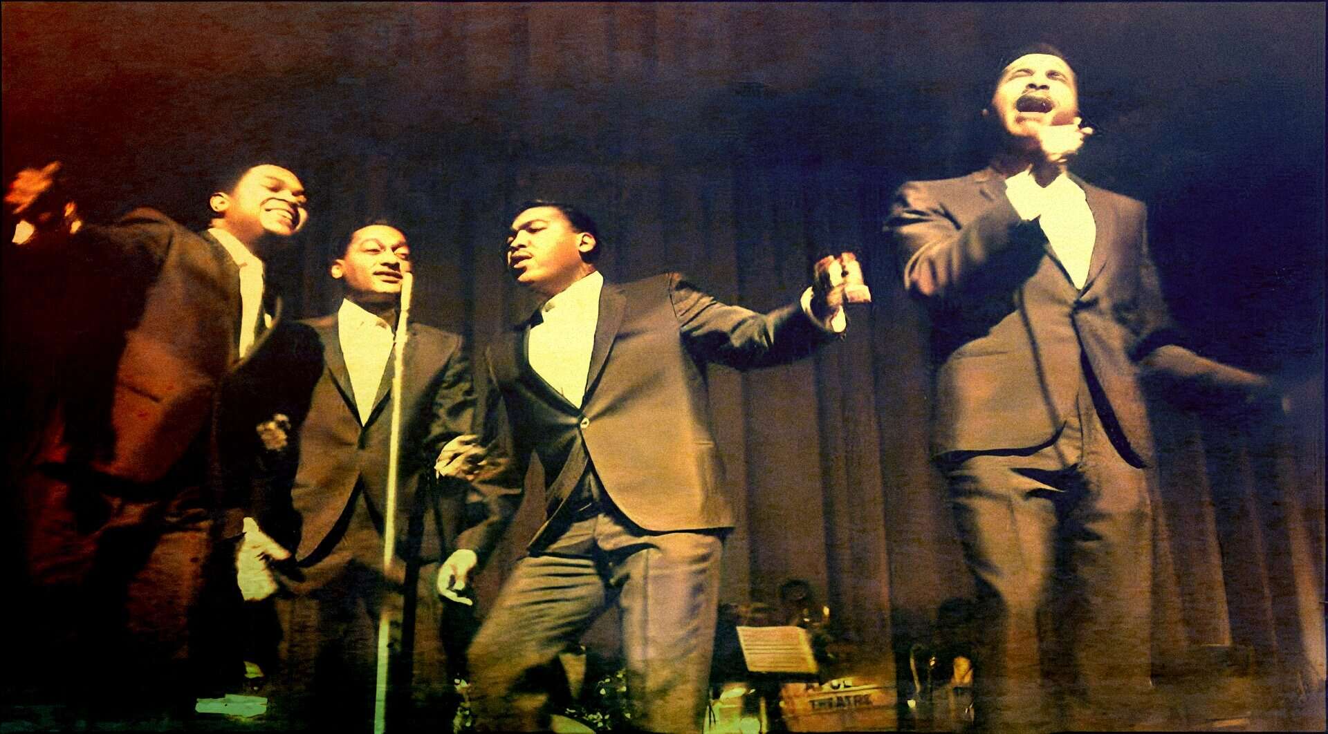 Vintage black and white photograph of four singers performing passionately on stage, showcasing classic doo-wop or early rock 'n' roll music, emphasizing lively historical music archive imagery.