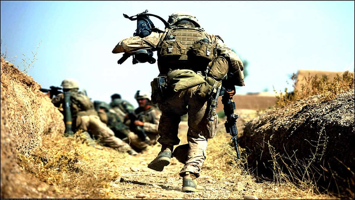 Soldiers in combat gear walking through a dirt path in a military operation.