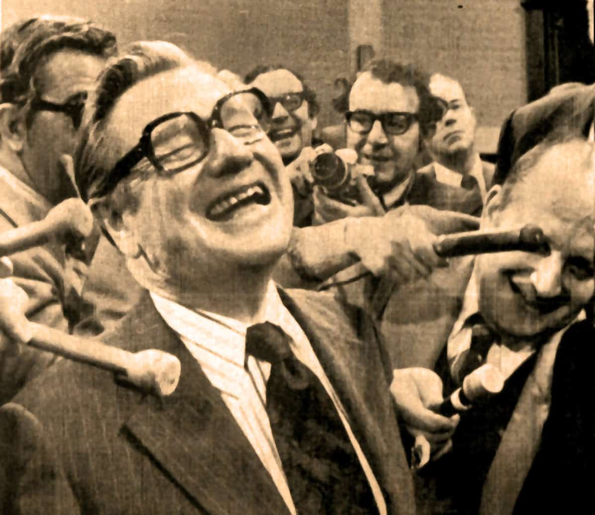 Vintage black-and-white photo of a man surrounded by reporters and journalists, capturing a lively news moment in the history of media coverage and broadcasting.