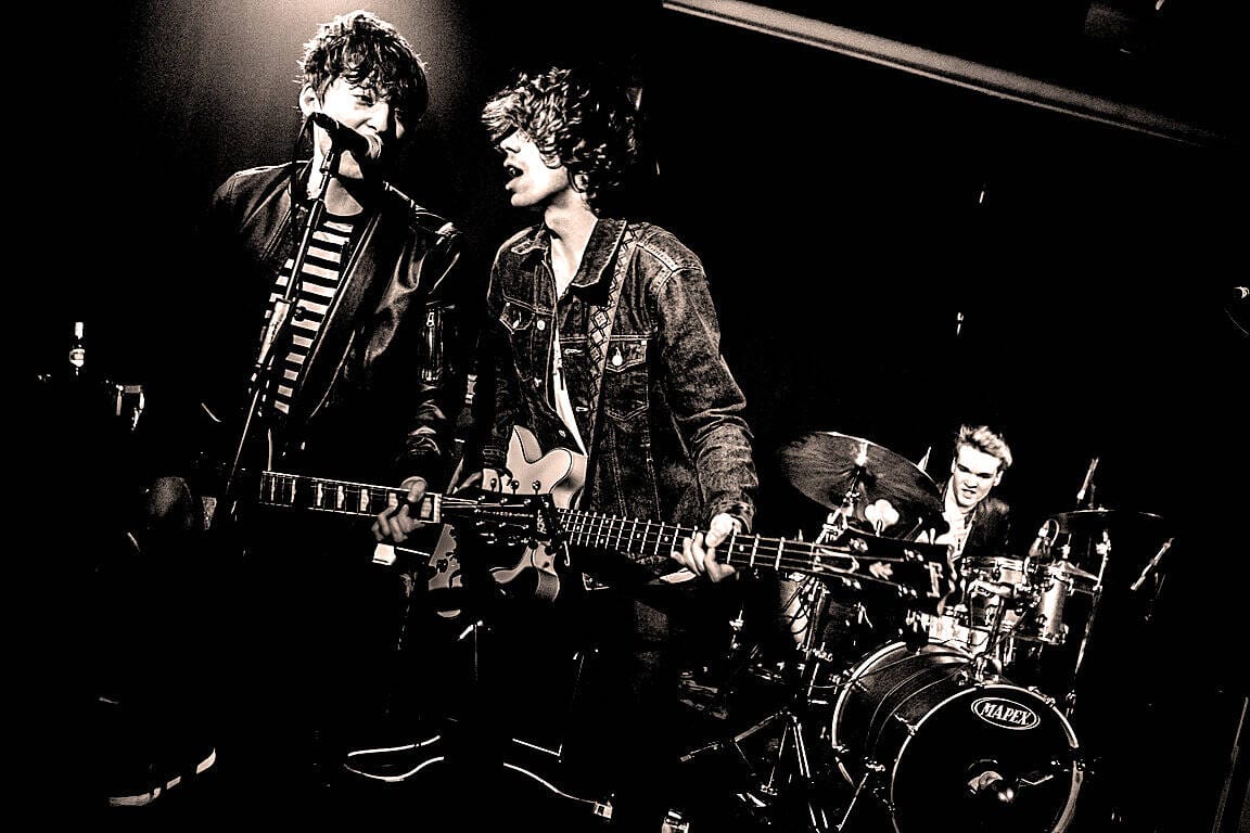 Energetic rock band performing live on stage with guitars and drums at a music event.