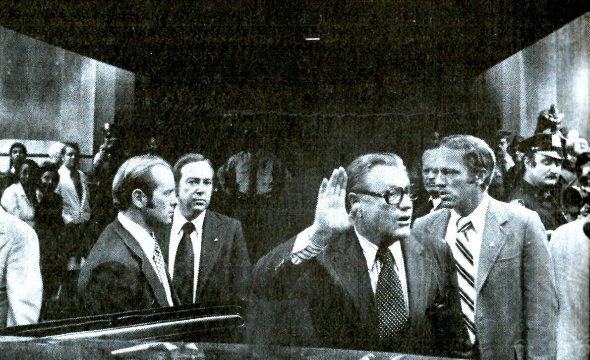 A sound archive image showcasing a historical political event with a man taking an oath or making a public statement, surrounded by journalists and officials, emphasizing news, history, and political communication.