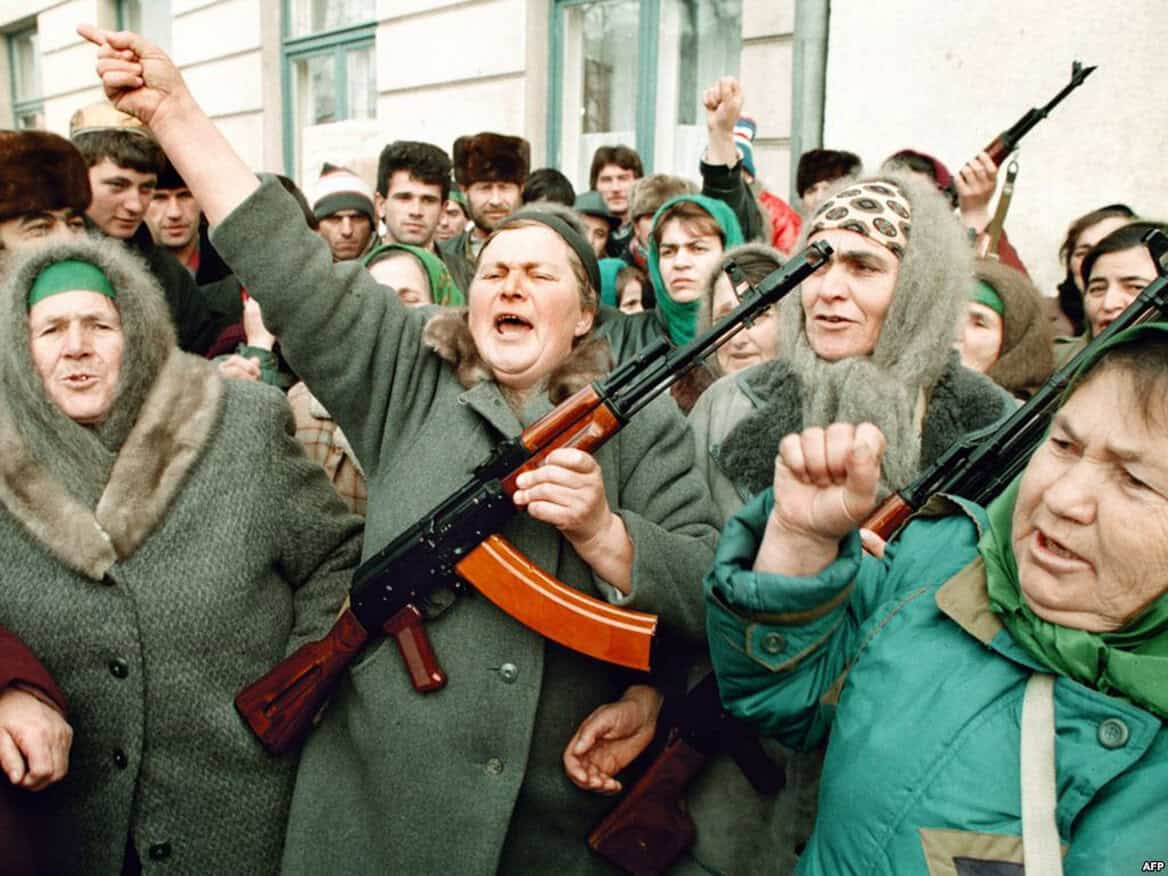 Protesters with rifles in a crowded street demonstrating during a political rally, capturing history and news relating to Cold War tensions and civil unrest.