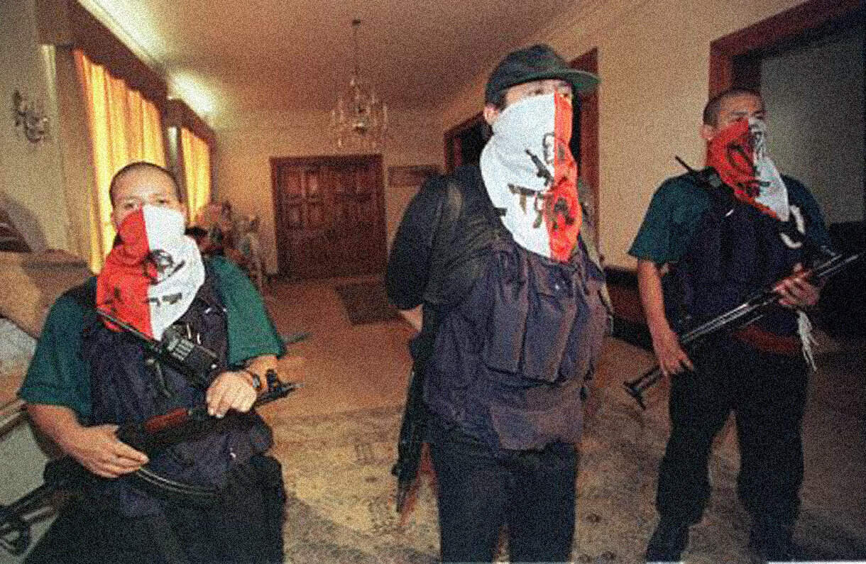 Masked individuals with guns in a home setting, depicting a tense or criminal scenario, possibly related to protests or illegal activities. Image from Past Daily news and music archive.
