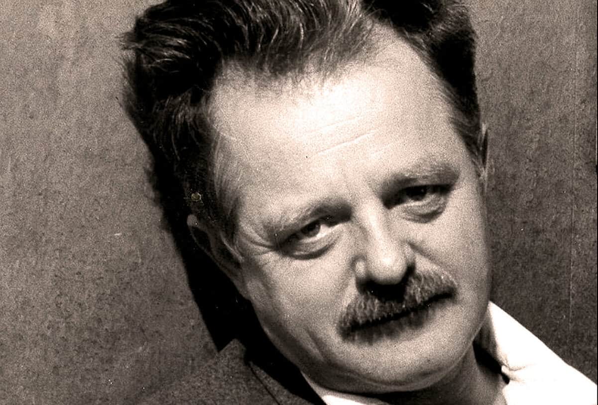 Close-up black and white portrait of a man with a mustache, highlighting classic 20th-century American music and news history.