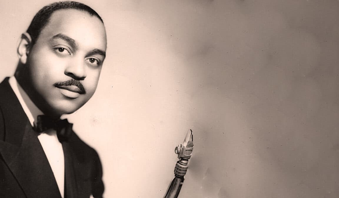 Vintage black and white photograph of a man in a tuxedo with a bow tie, featuring a robotic arm, representing historical sound archive recordings of news, music, and history at Past Daily.