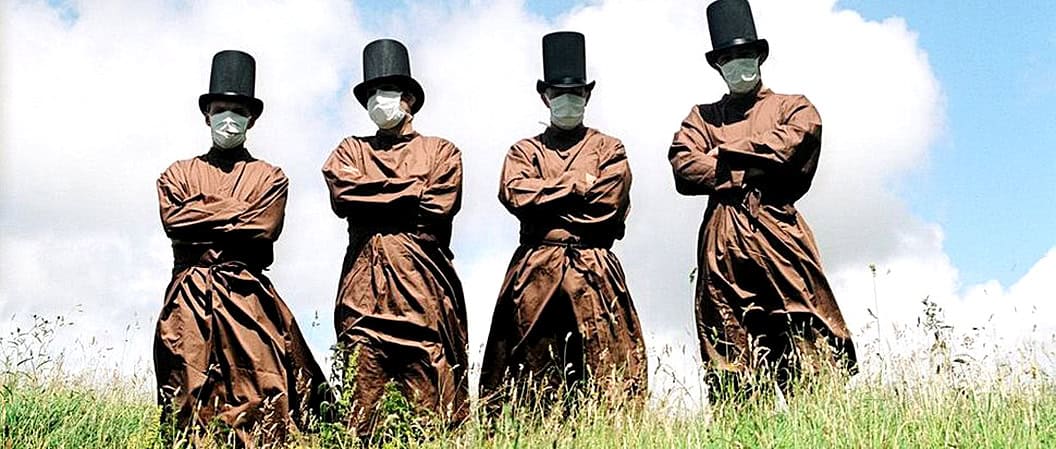 Clergy members wearing face masks and traditional attire standing in a grassy field during daytime, reflecting historical and cultural significance.