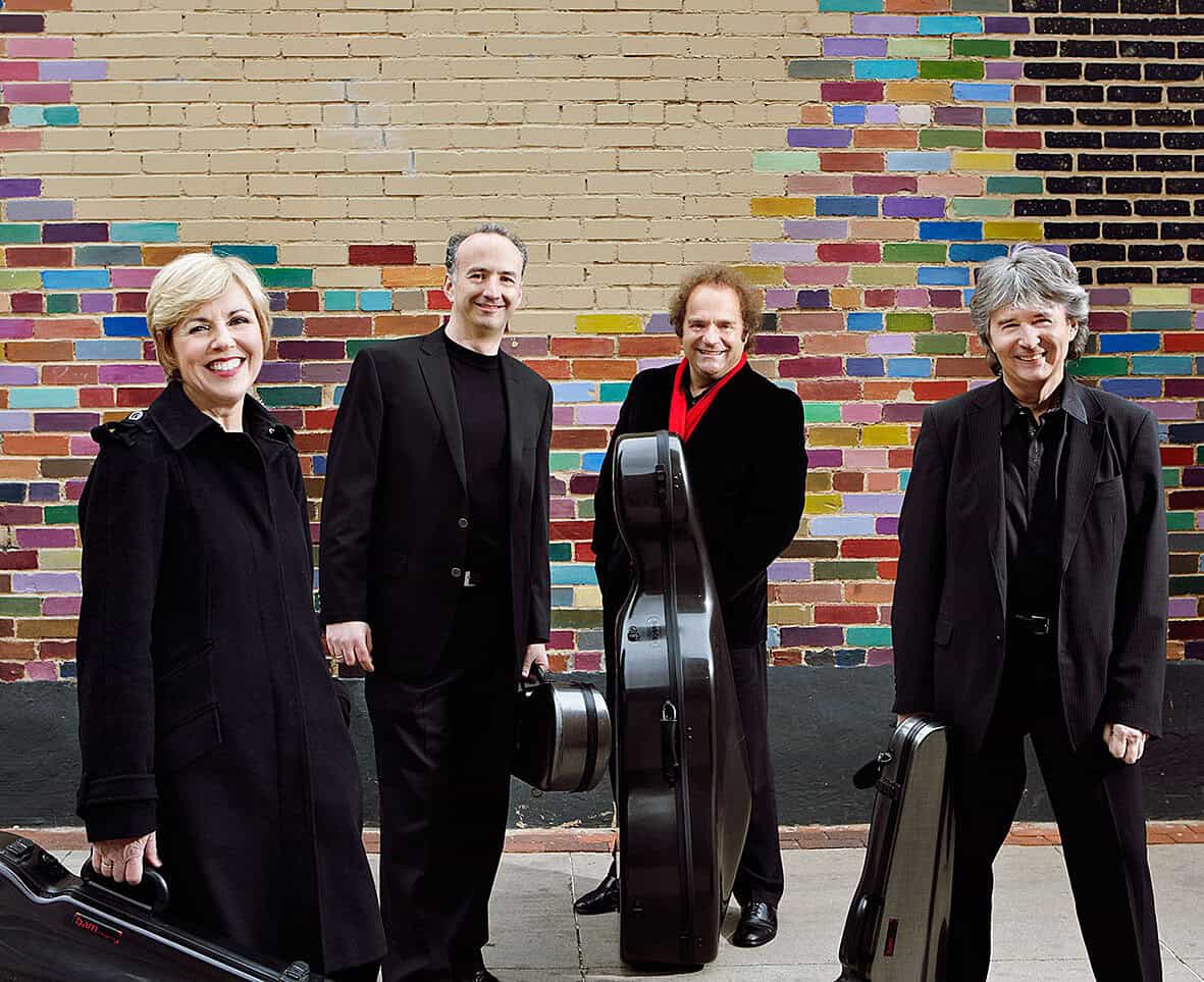 People with musical instruments standing in front of a colorful brick wall, representing a music band or performance scene.