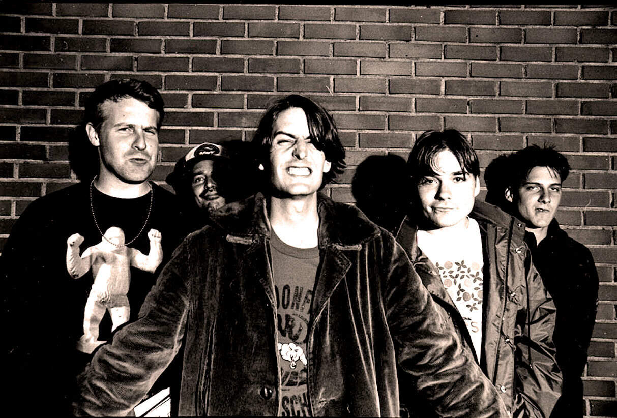 Rock band portrait black and white, musical artists, edgy group photo, alternative music, band members with brick wall background, nostalgia for classic rock, musicians in a candid shot, indie band imagery, musical history, Past Daily archive relevance.