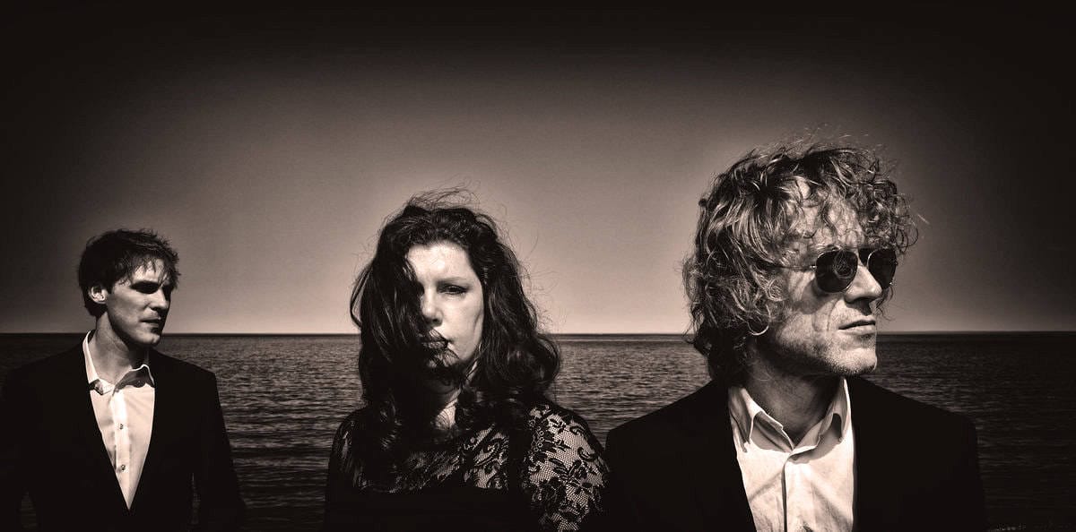 Vintage rock band photo featuring three musicians by the ocean, capturing raw musical artistry and nostalgia; perfect for music, history, and sound archive themes.