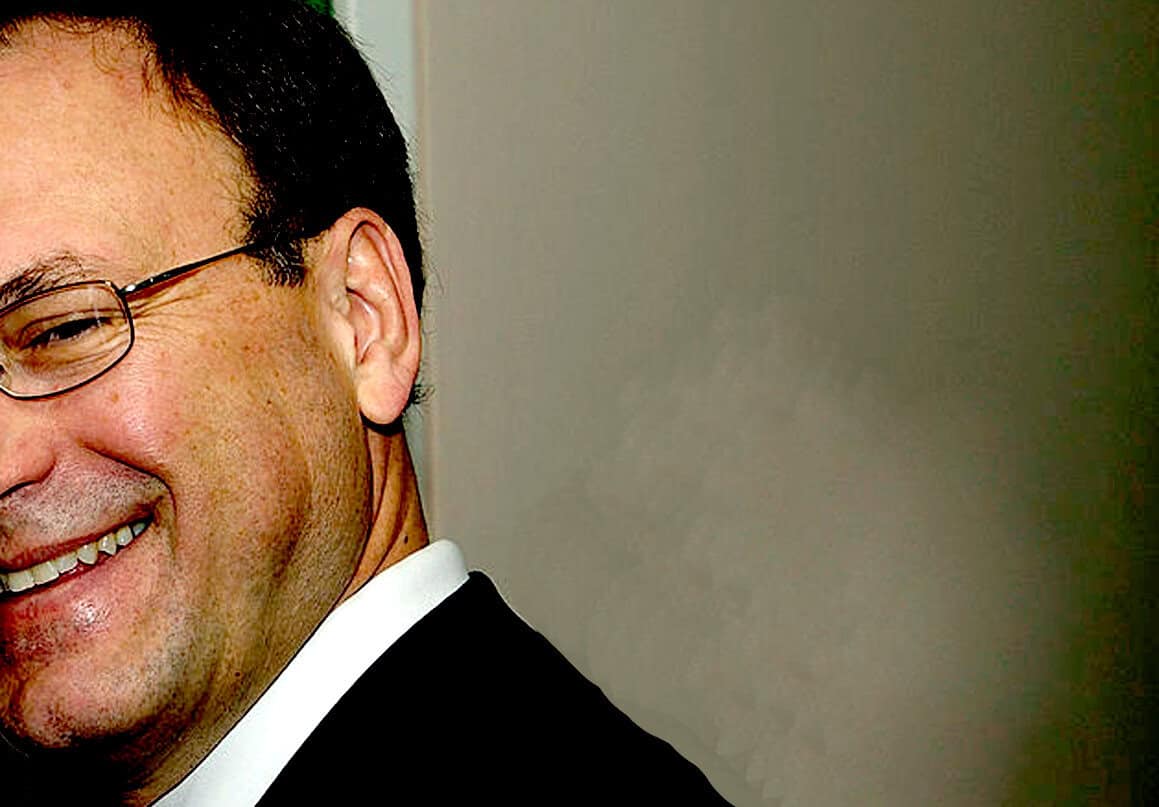 Smiling man in formal attire with glasses, representing news, history, and music archive themes from Past Daily.