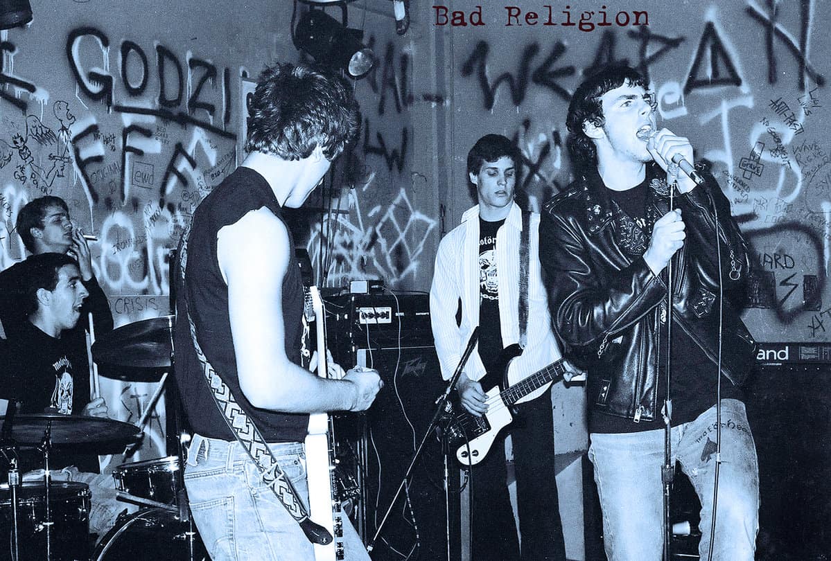 Black and white photo of a punk rock band performing live with graffiti-covered walls in the background, capturing raw energy, rebellious attitude, and underground music culture, related to music history.