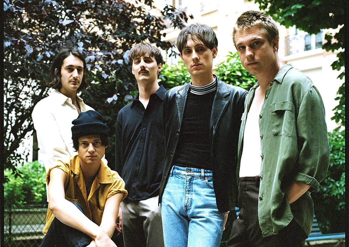 New wave band members outdoors, 1980s style, casual fashion, urban background, vintage music scene, alternative music scene, 80s fashion, indie band, group portrait, music history.