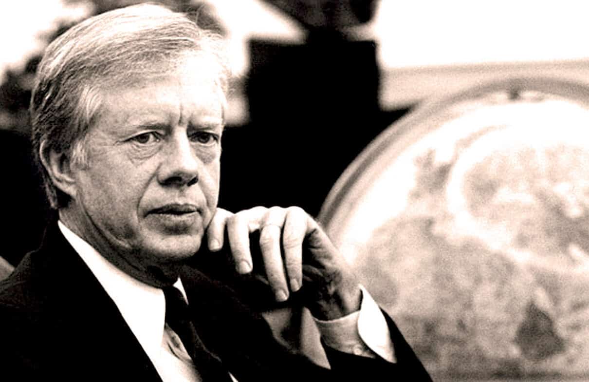Historical black and white image of a serious man in a suit with a globe in the background, representing news archives and historical recordings.
