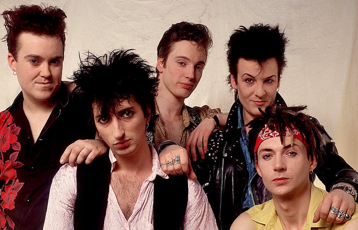 Vibrant 1980s glam rock band posed together, showcasing iconic hairstyles and fashion reflecting the influence of music history and pop culture from that era.