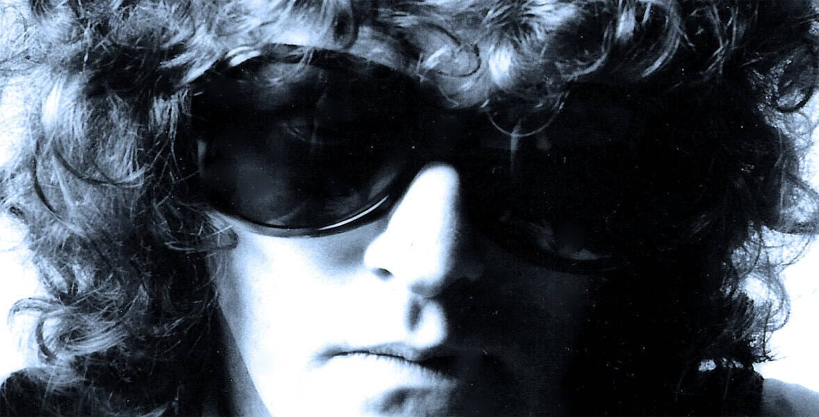 Vintage black and white close-up photo of a person with curly hair wearing dark sunglasses, symbolizing music, news archives, and historical sound recordings for Past Daily.