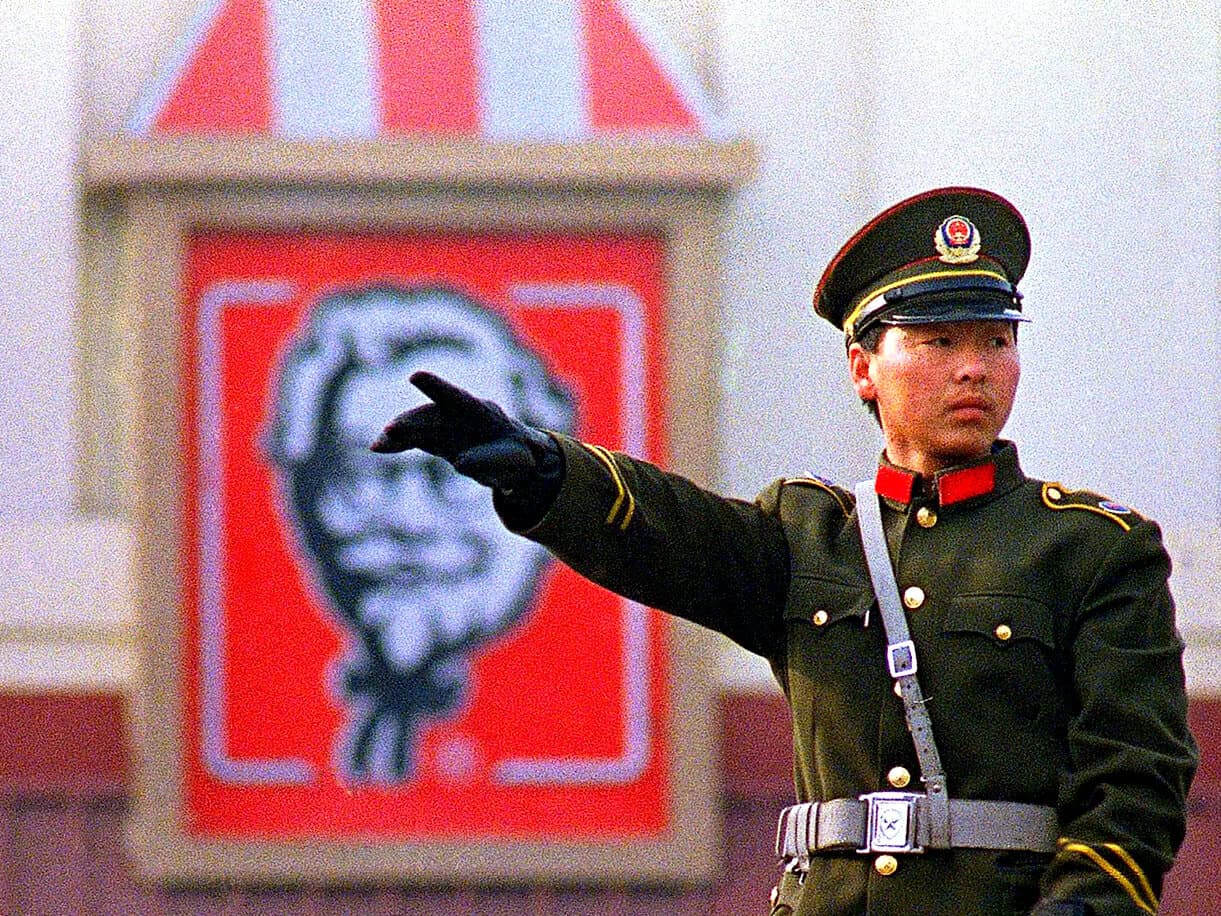 Military officer in uniform pointing, with Mao Zedong portrait in the background, symbolizing Chinese history, politics, and cultural heritage.