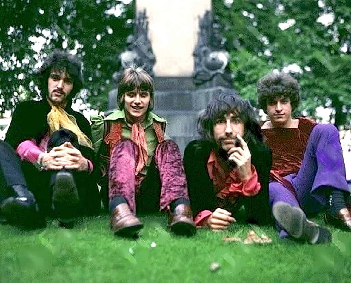 Colorful vintage band members sitting outdoors in front of a monument, showcasing 1960s music culture and style.
