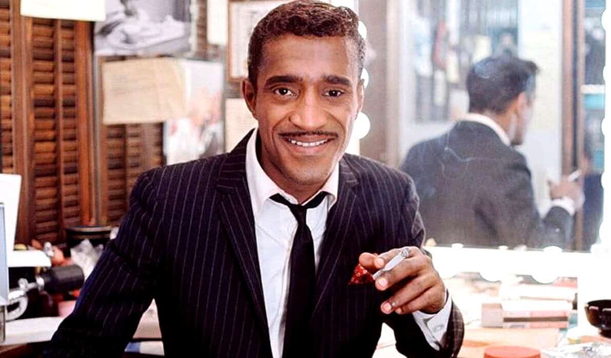 A sophisticated man in a pinstripe suit smiling in a stylish cafe setting, showcasing vintage ambiance and classic fashion.