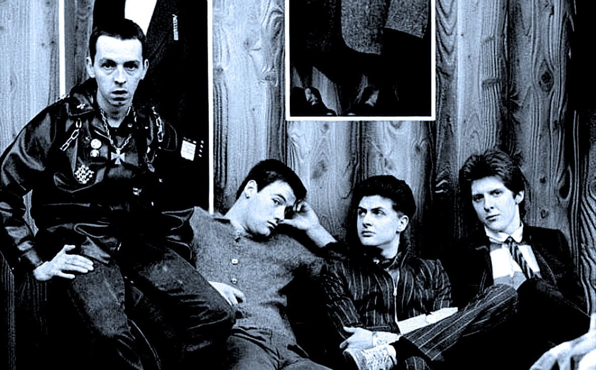 Teenagers sitting in a room with wood-paneled walls, in a black-and-white photo, capturing youth culture, music, and rebellious attitudes, related to iconic music or pop culture moments.