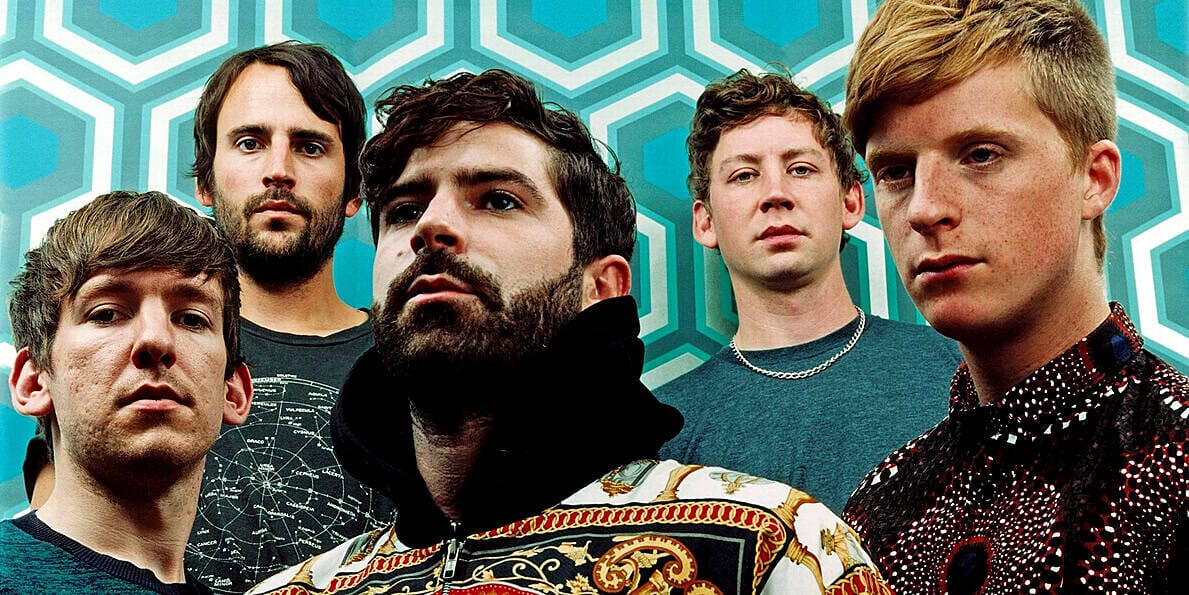 Vampire Weekend band members posing for a promotional photo with geometric patterned background, highlighting indie rock music and band photography.