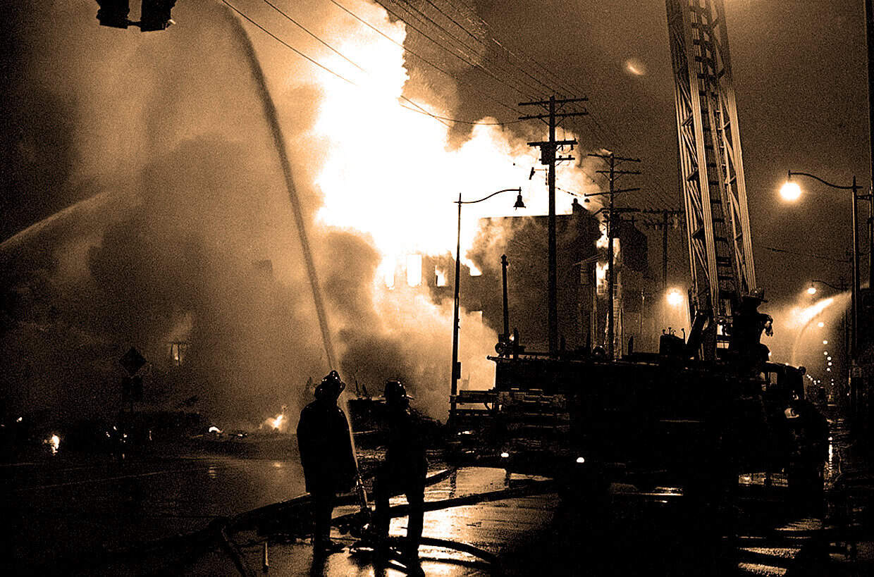 Explosion fire incident in urban area during night, firefighters battling blaze, emergency response, city street, dramatic scene, smoke and flames, disaster management, fire truck, firefighting equipment.