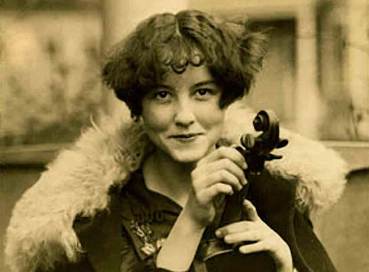 Female vintage photographer holding a camera in black and white, classic photo capturing history, music, news, archival image of media and journalism, nostalgic historical photo, Past Daily sound archive relevance.