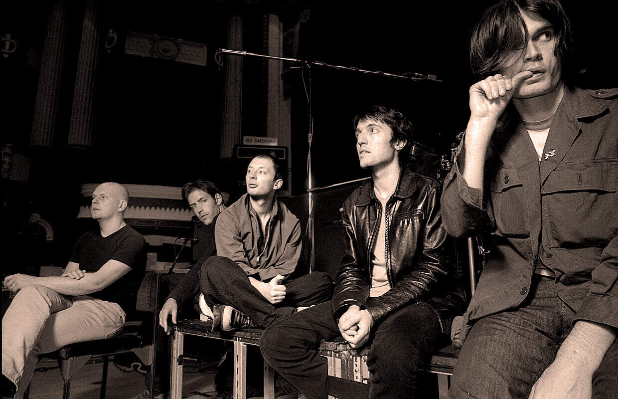 Archive photo of a band seated in a recording studio, capturing a moment during a music production session, highlighting the historical significance of musical history and sound archives.